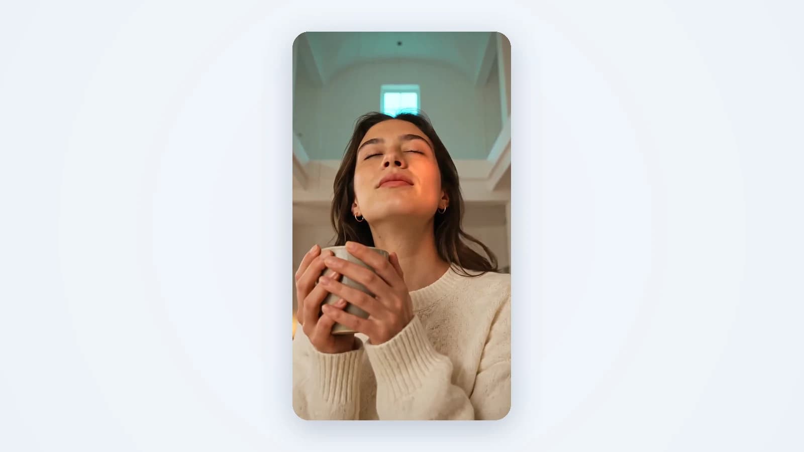 A vertical 9:16 video frame: a woman holds a warm mug with her eyes closed in soft window light