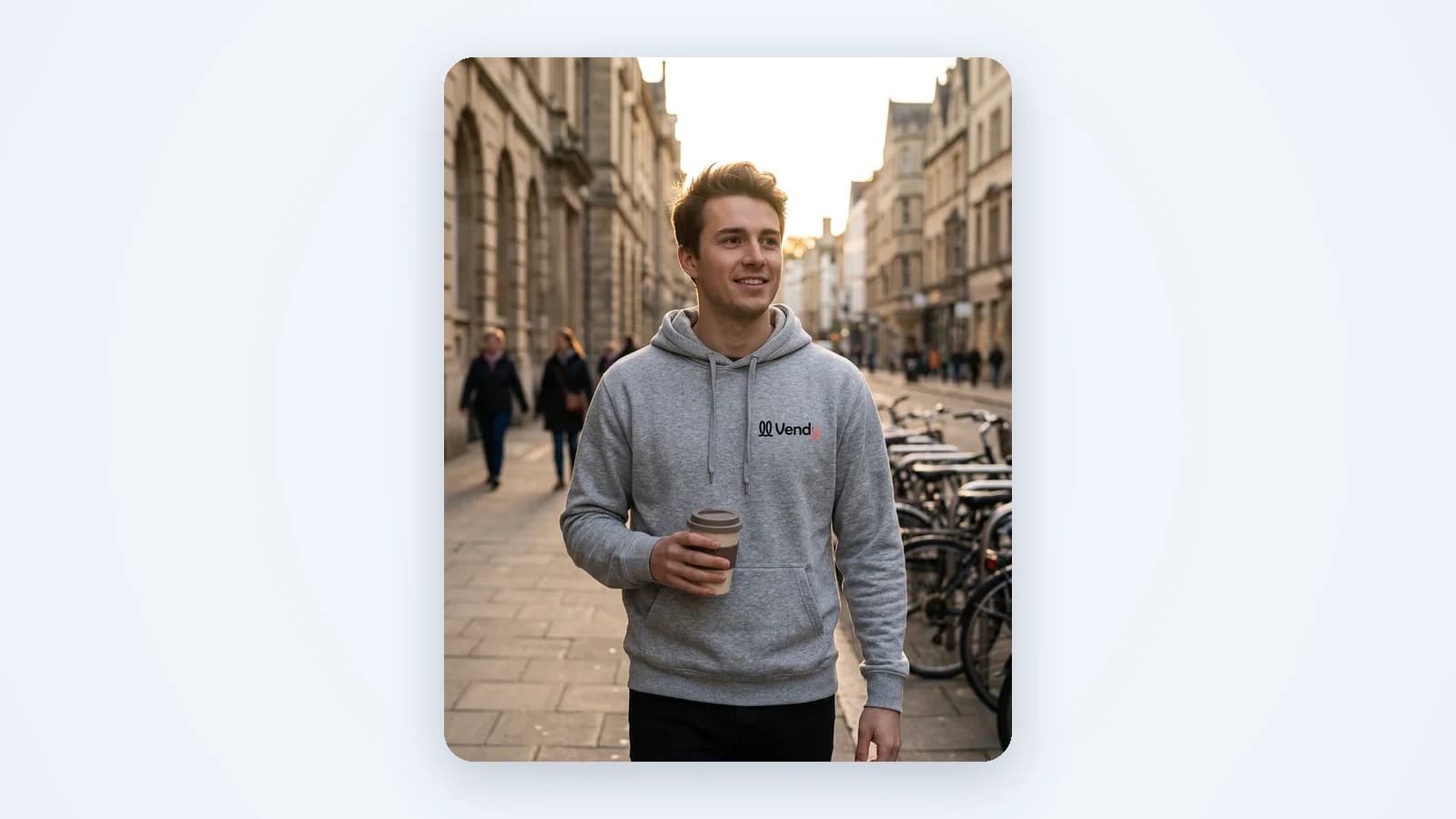 A vertical, phone-shot frame: a man walks down a city street in a branded hoodie with a coffee in hand