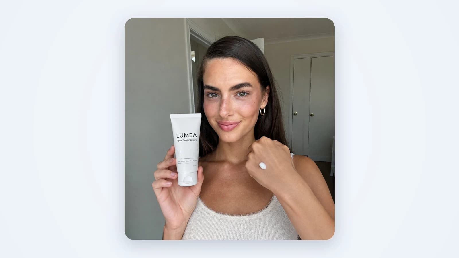 A creator holds a tube of cream to the phone camera with a dab of it on her hand, shot at home