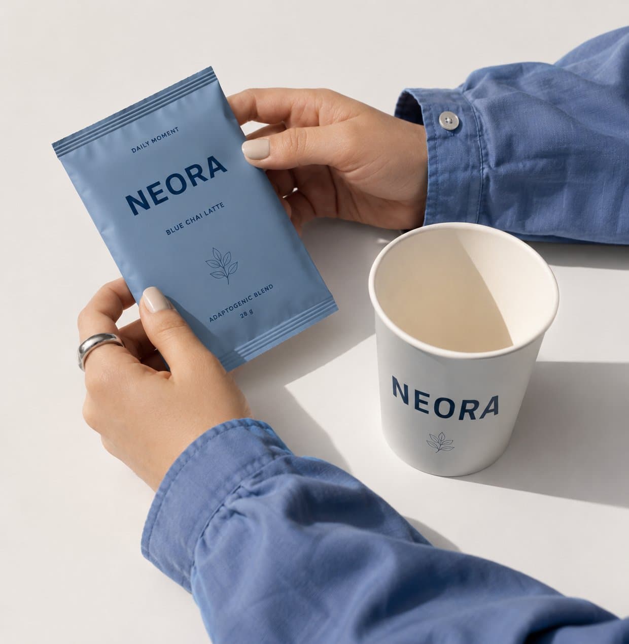 Hands placing a Neora sachet beside a cup in a lifestyle scene